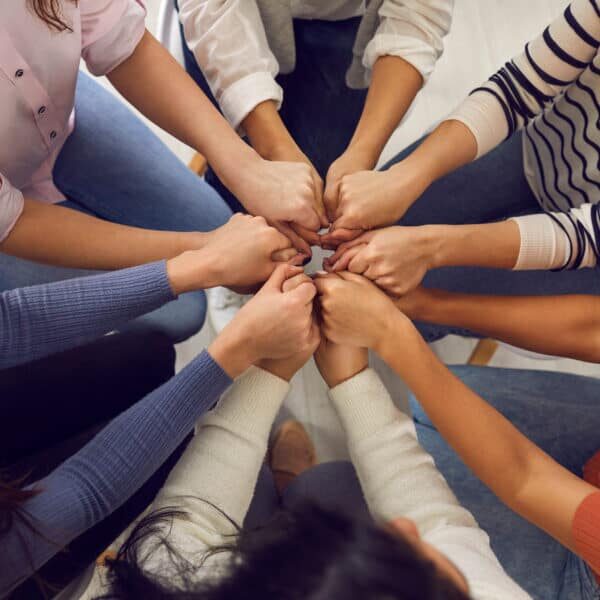 Top view close up of women's hands holding each other in group therapy or in a session with a motivational trainer. Concept of women's community, psychological help, trust and support.
